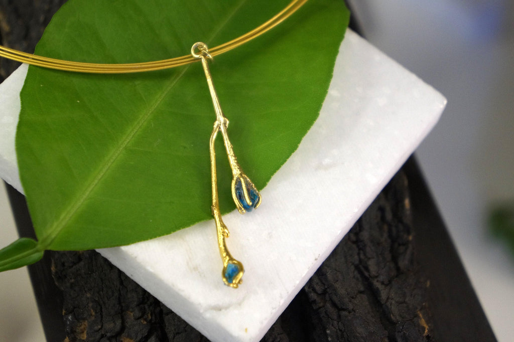 A gold necklace with a leaf-shaped pendant is displayed on a white surface.
