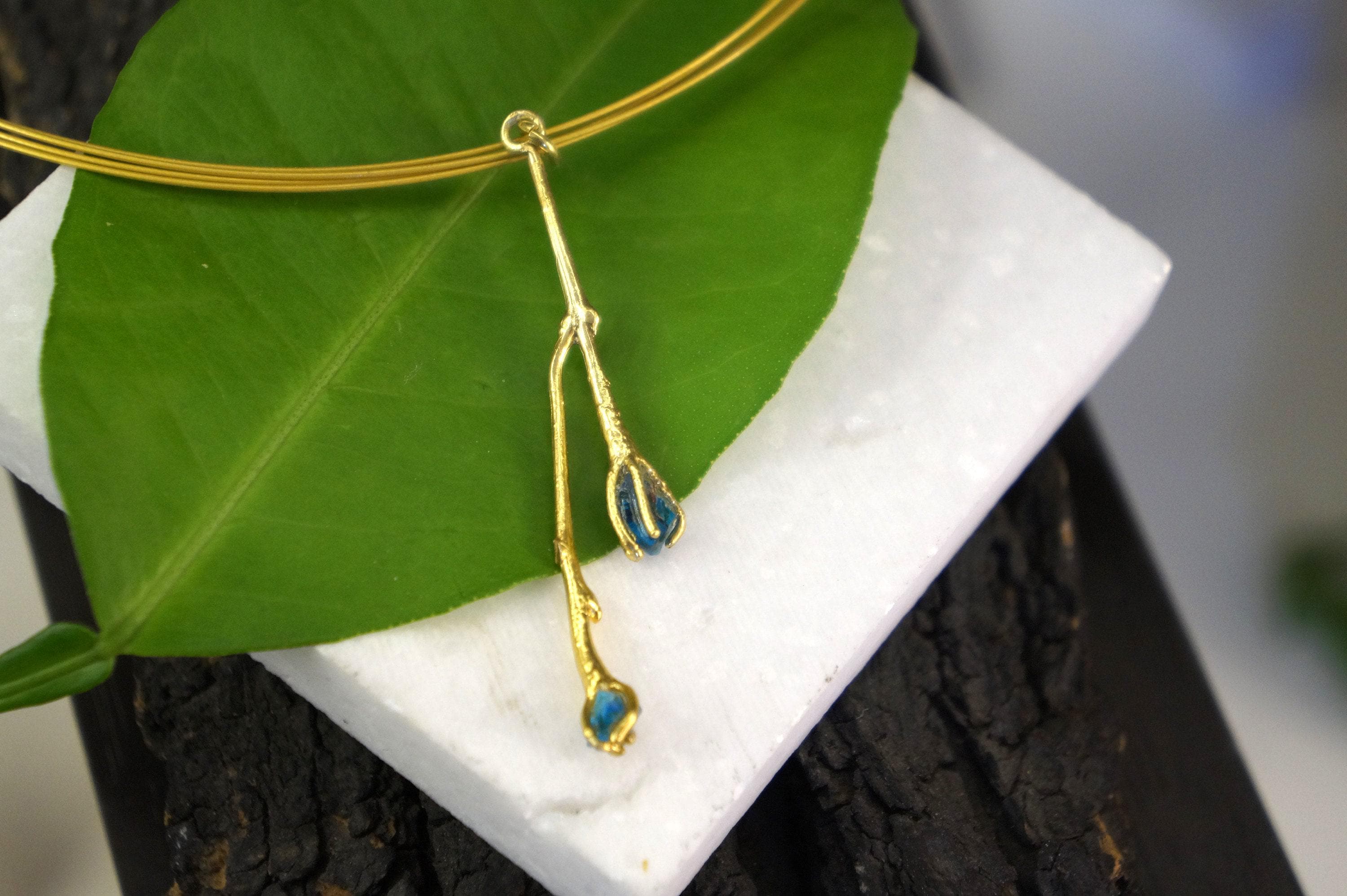A gold necklace with a leaf-shaped pendant is displayed on a white surface.