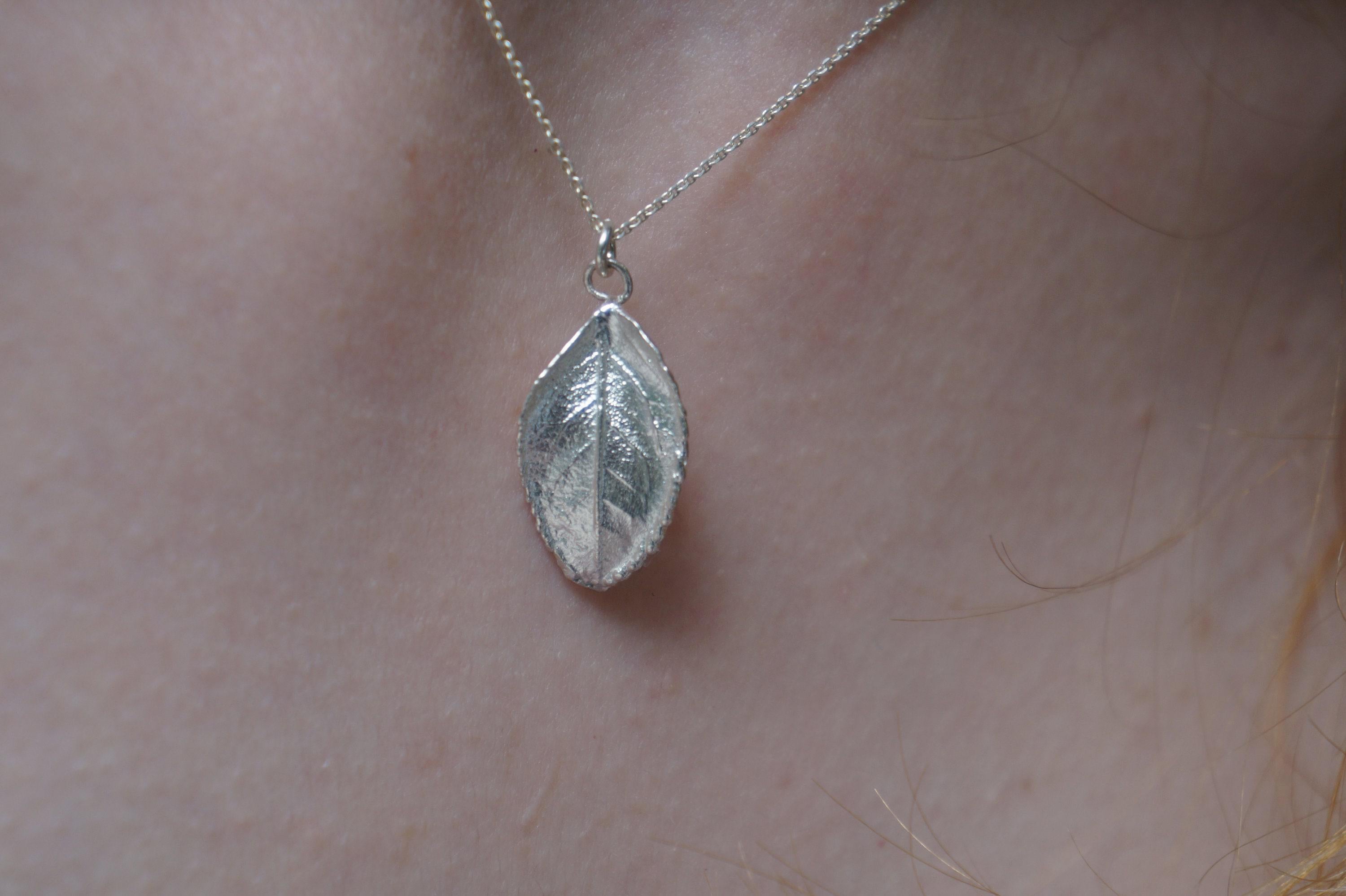 A silver leaf pendant necklace is worn around a person's neck.