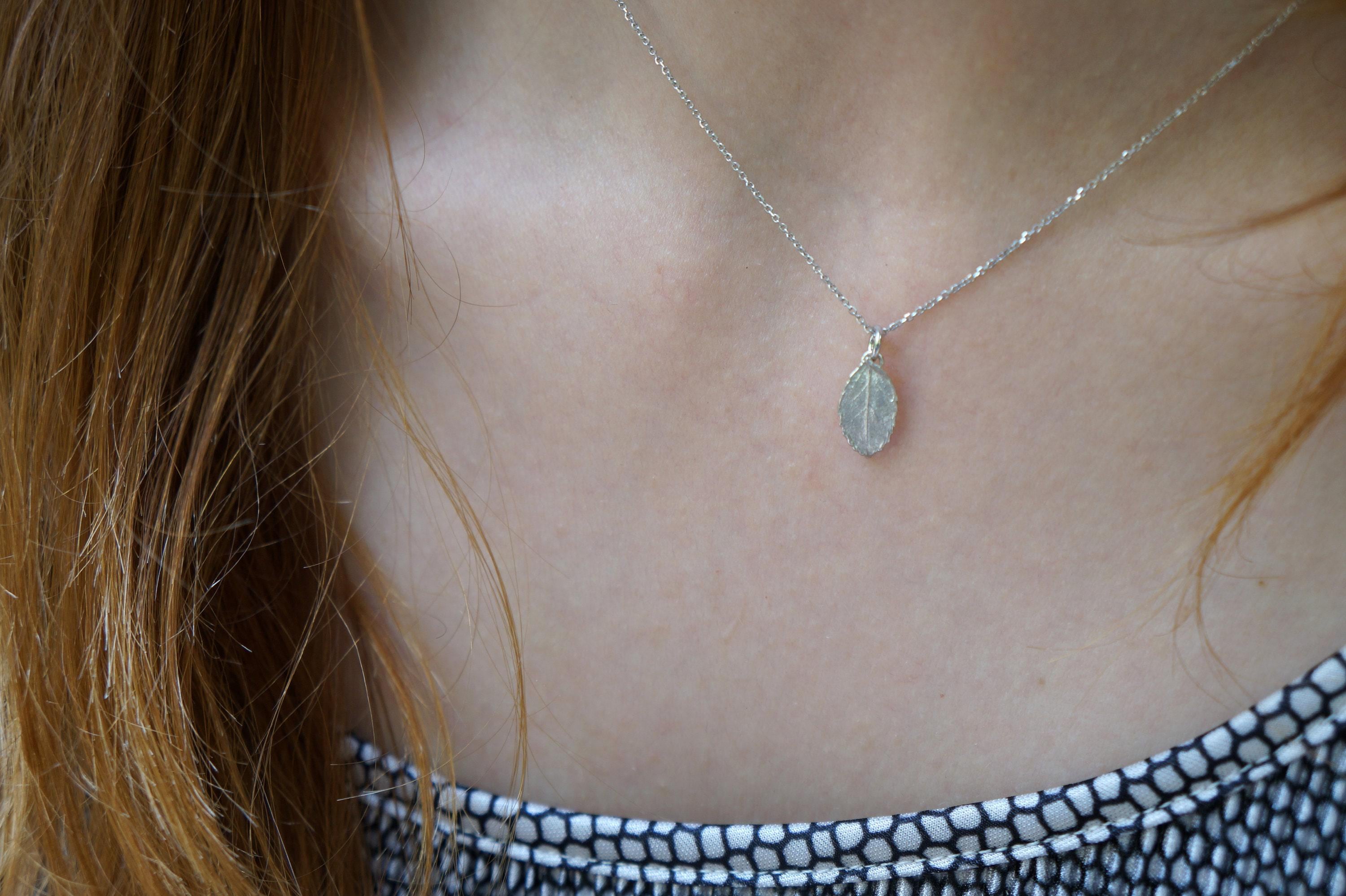 A close-up view of a person's neck and chest area, with a delicate silver necklace featuring a small leaf pendant.