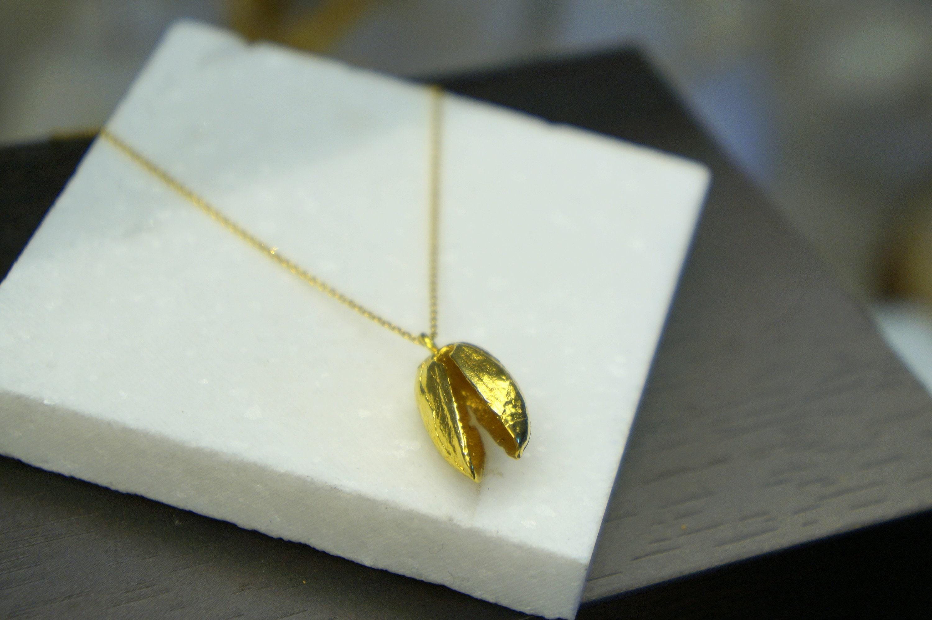 A gold necklace with a pendant in the shape of a leaf is displayed on a white foam surface.