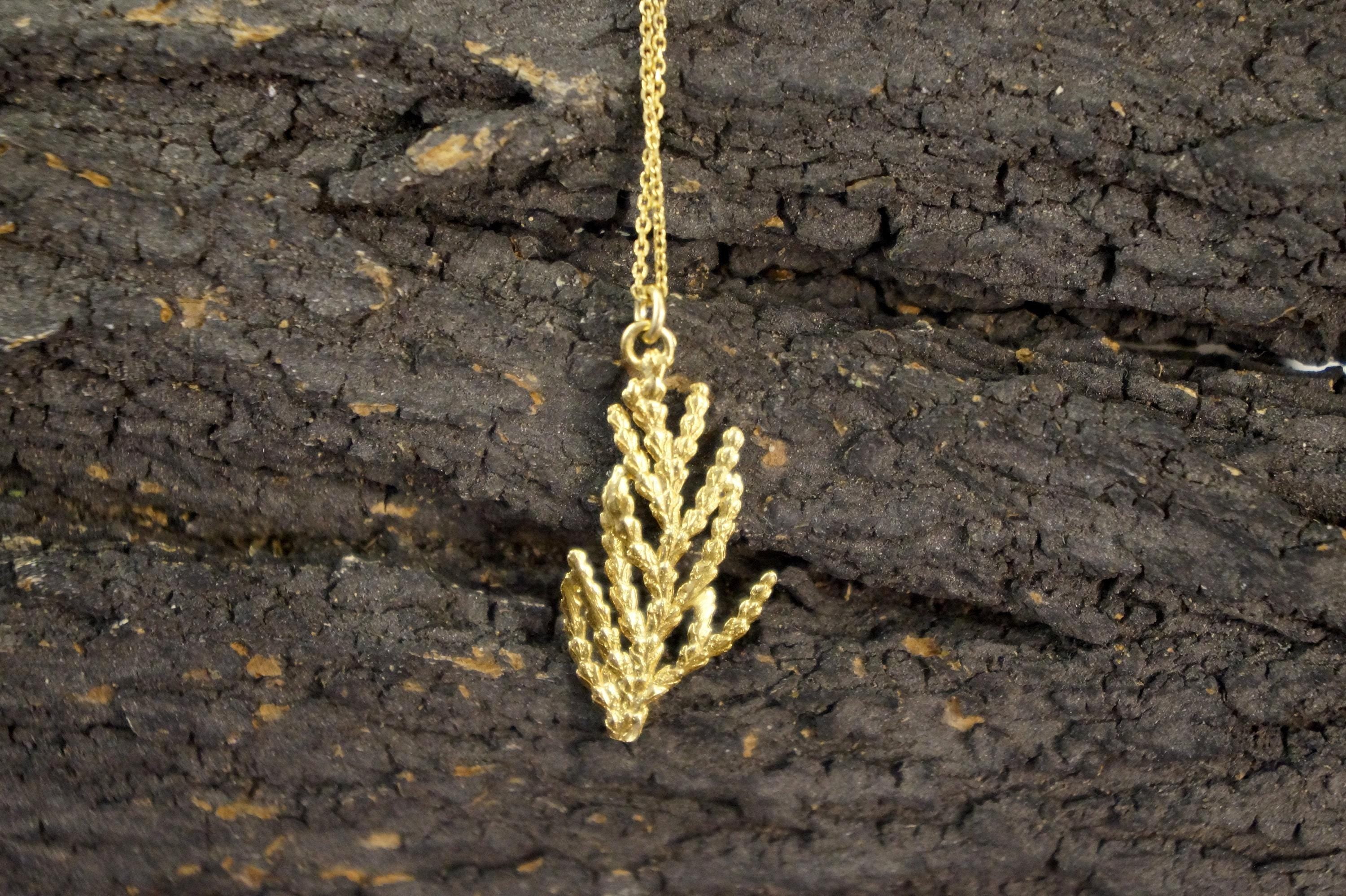 A gold-colored necklace with a leaf-shaped pendant is displayed against a dark, textured background.
