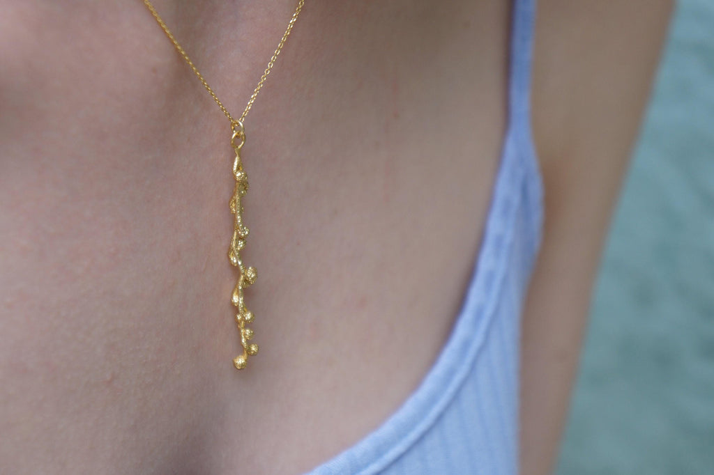 A close-up view of a gold necklace with a pendant hanging from a person's neck.
