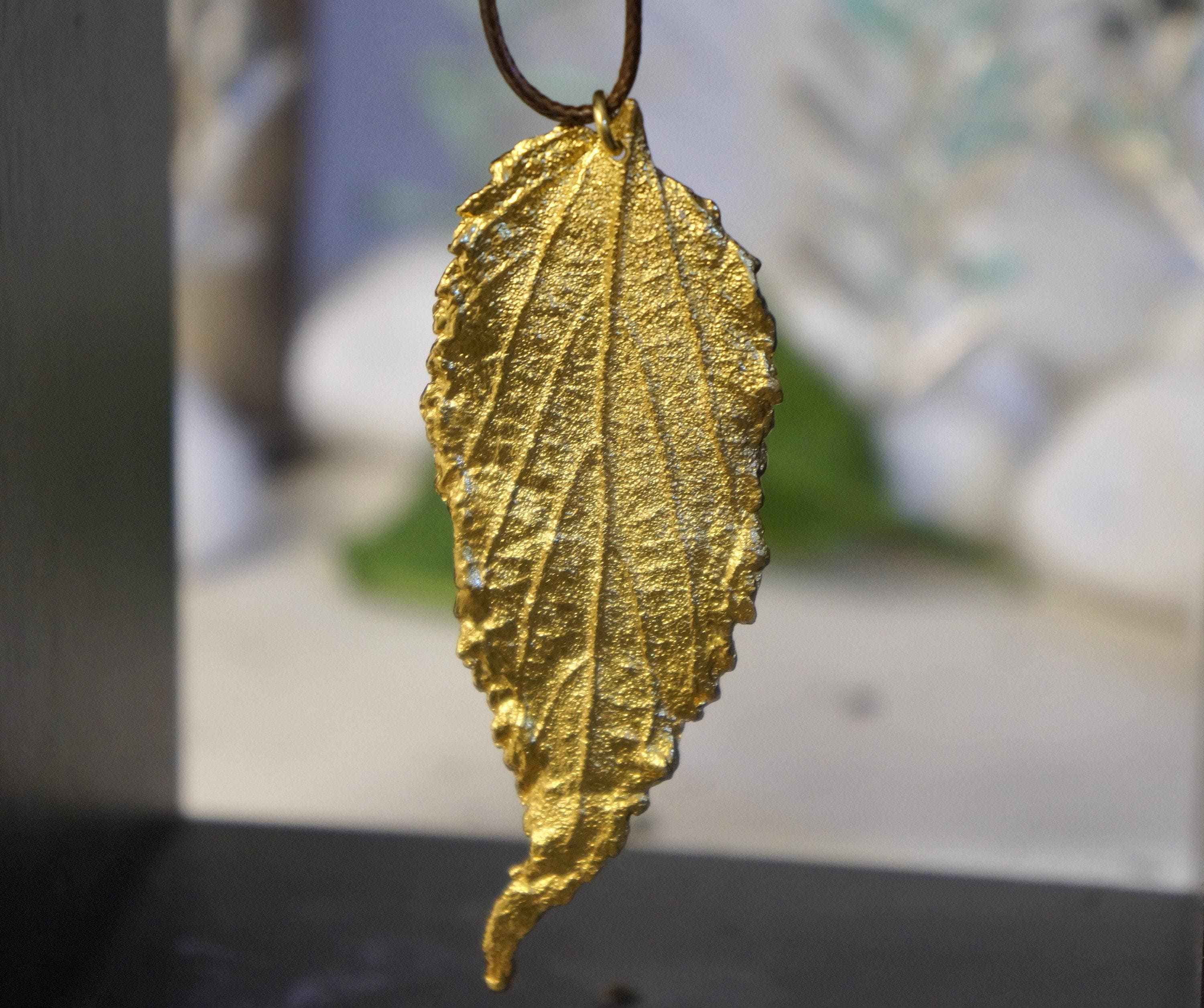 A close-up image of a gold leaf pendant hanging from a chain.