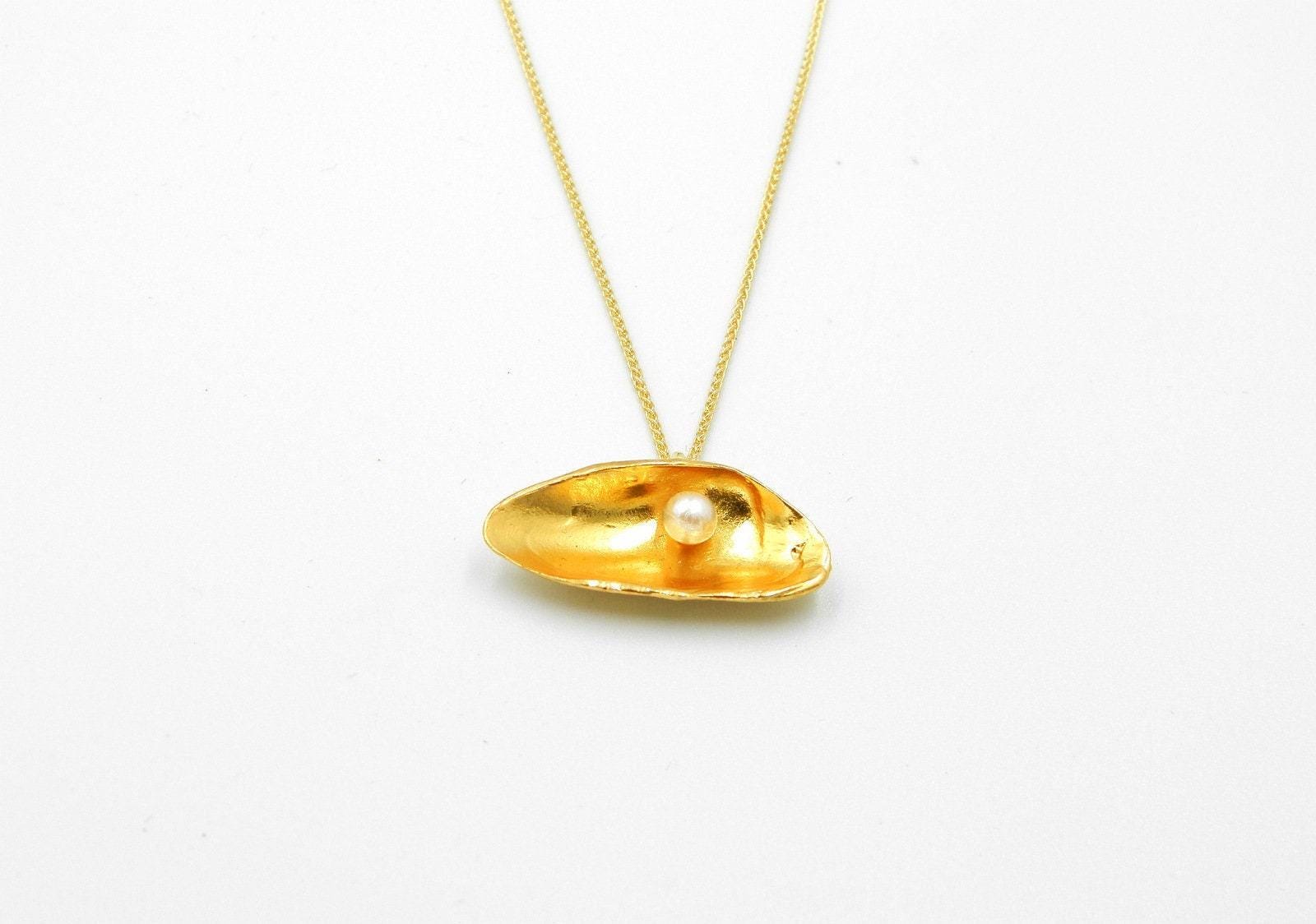 A gold necklace with a pendant in the shape of a shell, containing a single pearl.
