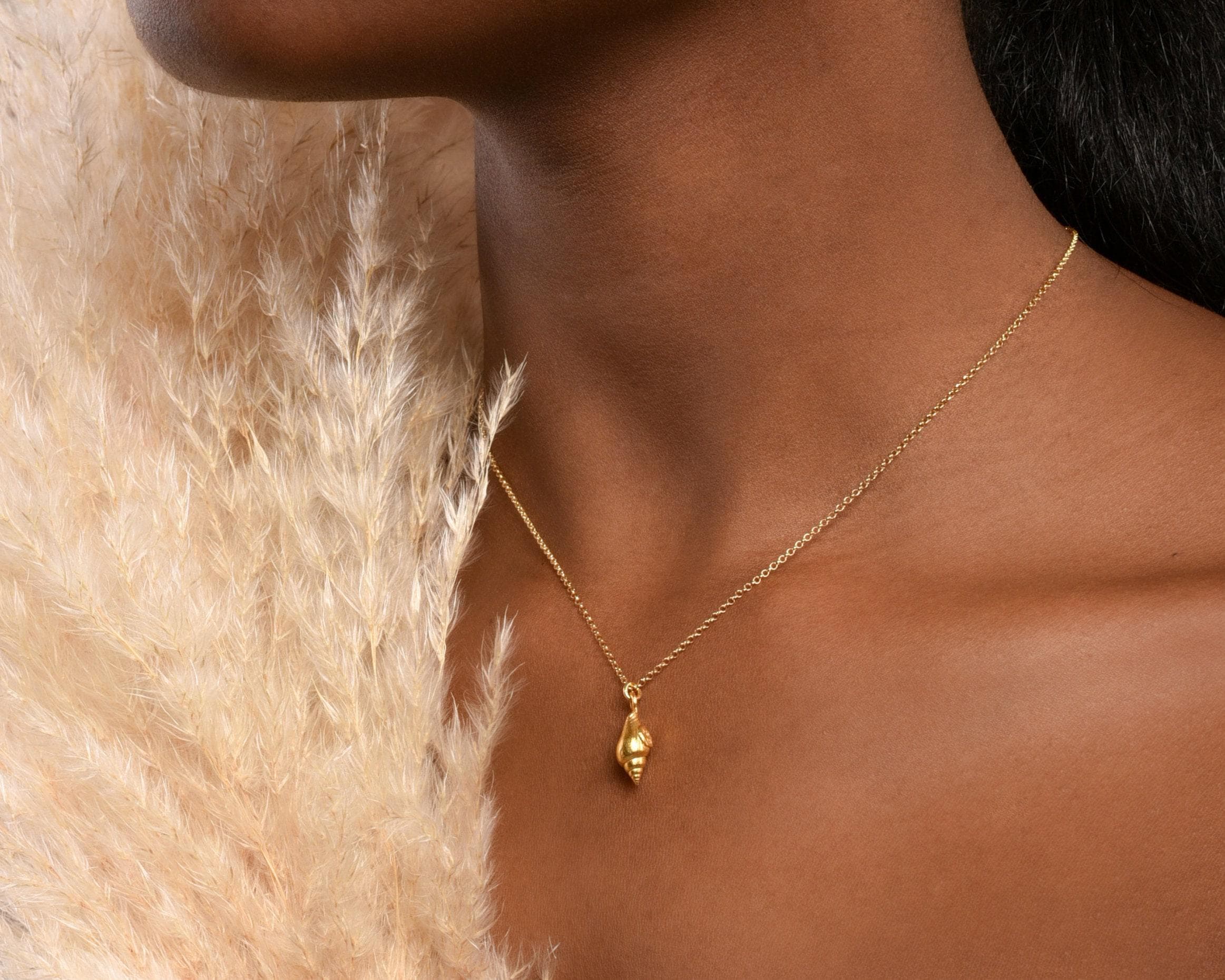 A close-up of a gold necklace with a pendant, worn by a person with a pensive expression.