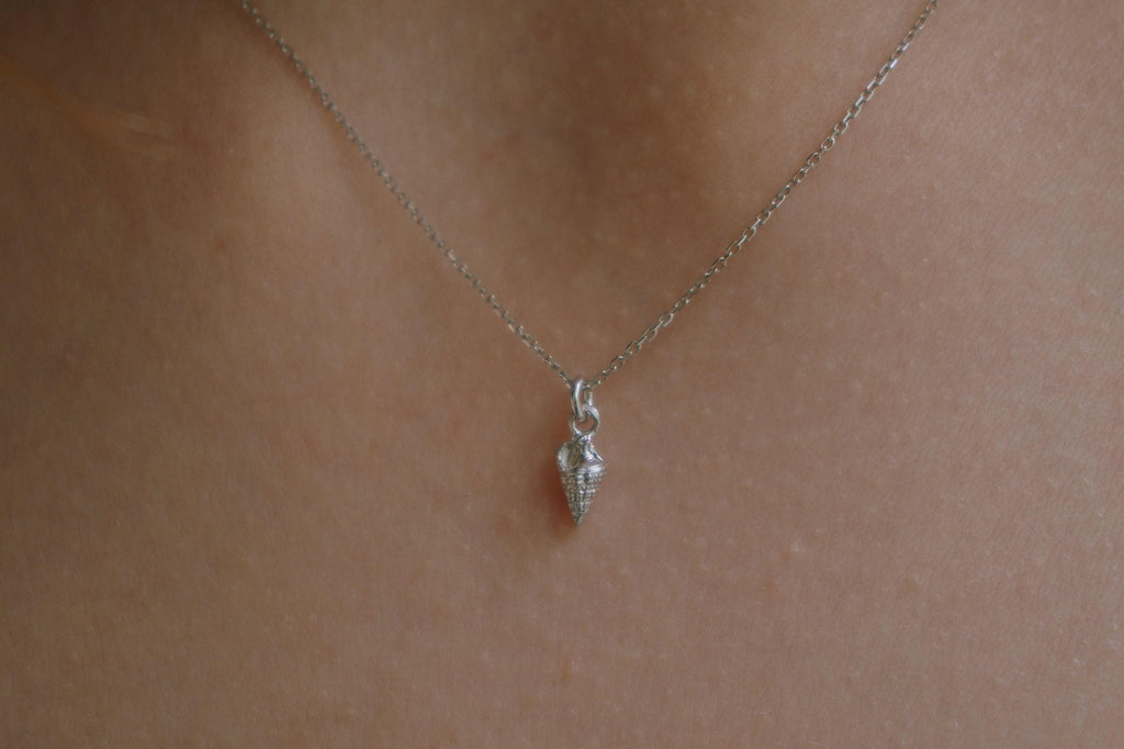 A delicate silver necklace with a small pendant is shown against a light brown background.