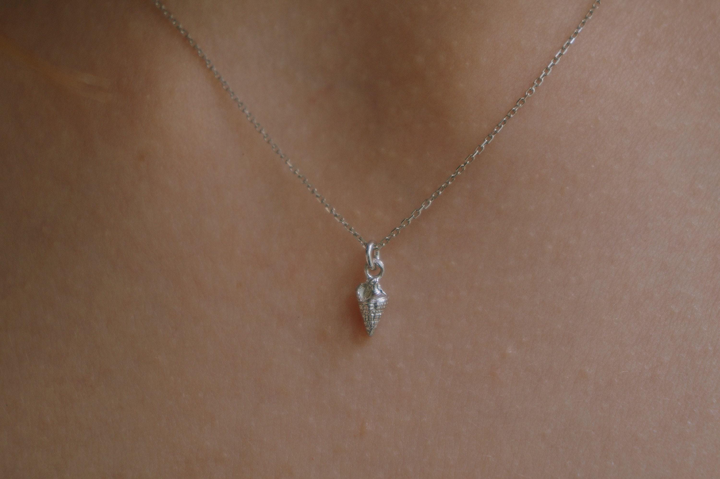 A delicate silver necklace with a small pendant is shown against a light brown background.