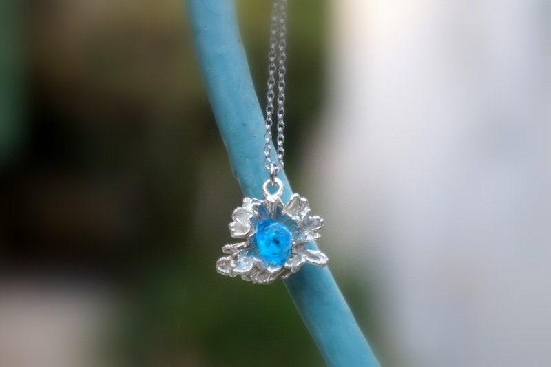 A delicate silver necklace with a blue gemstone pendant is suspended from a thin blue cord.
