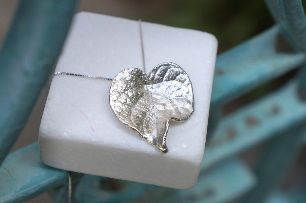 A white square box with a silver leaf pendant resting on top of it.