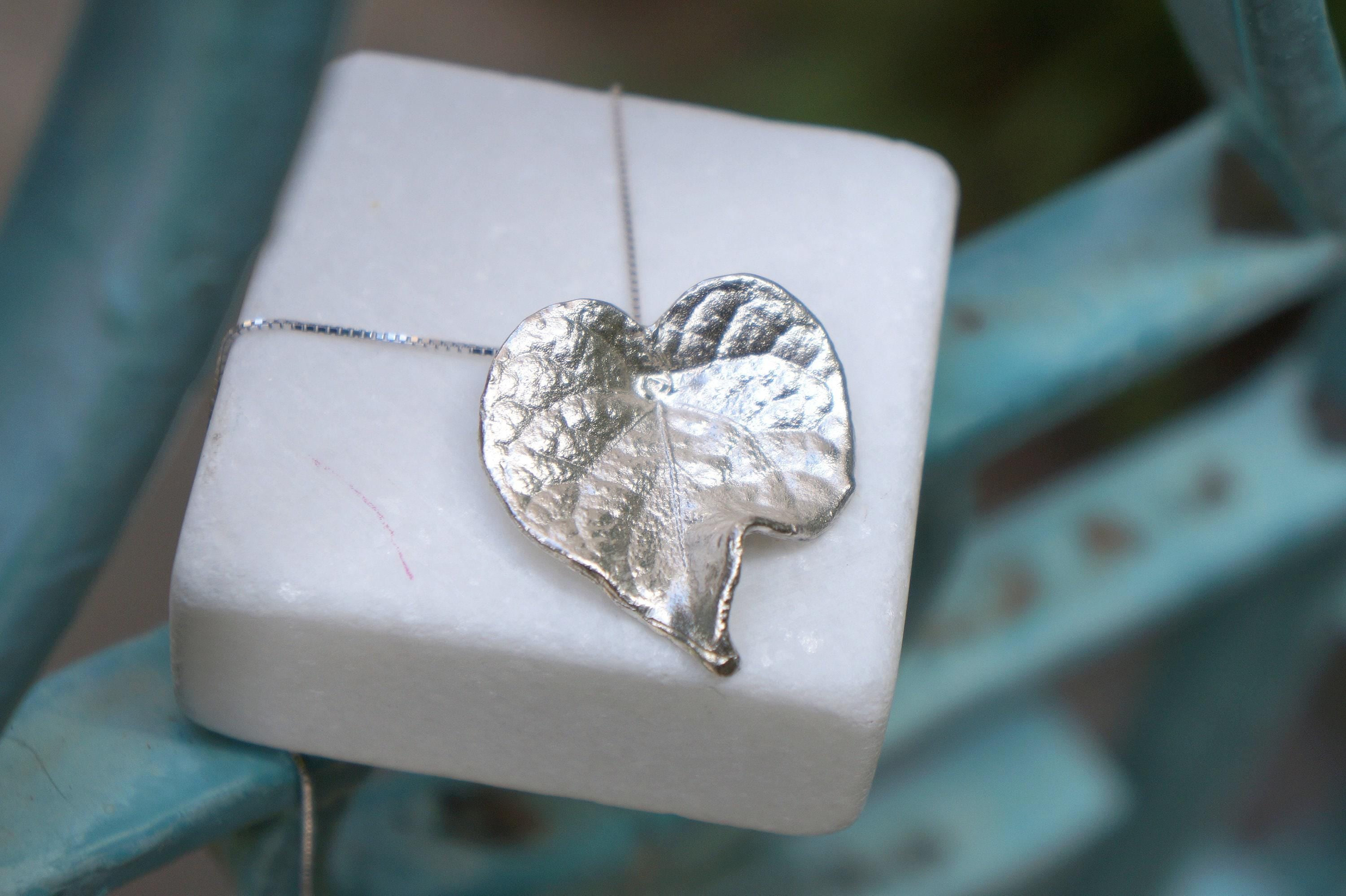 A white square box with a silver leaf pendant resting on top of it.