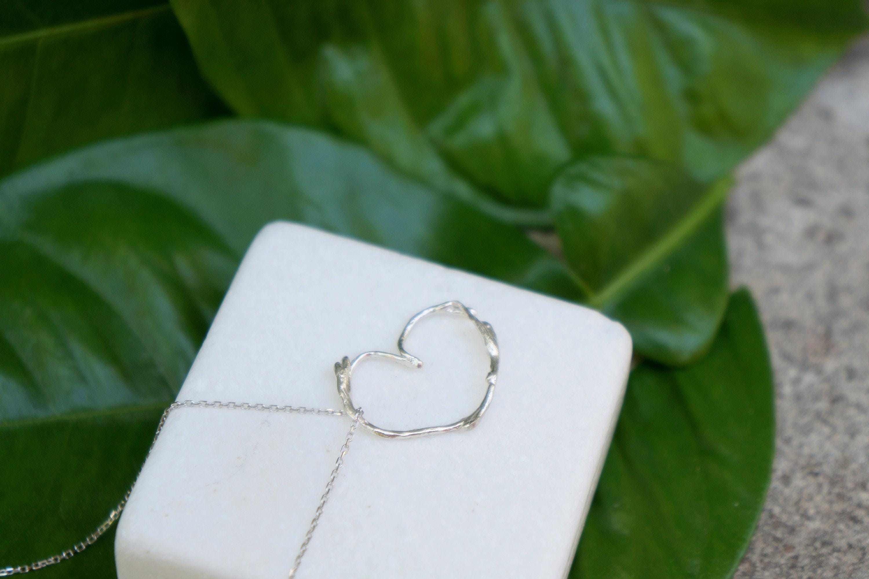 A heart-shaped pendant made of gold metal is displayed on a white marble surface, with a gold chain necklace around it.