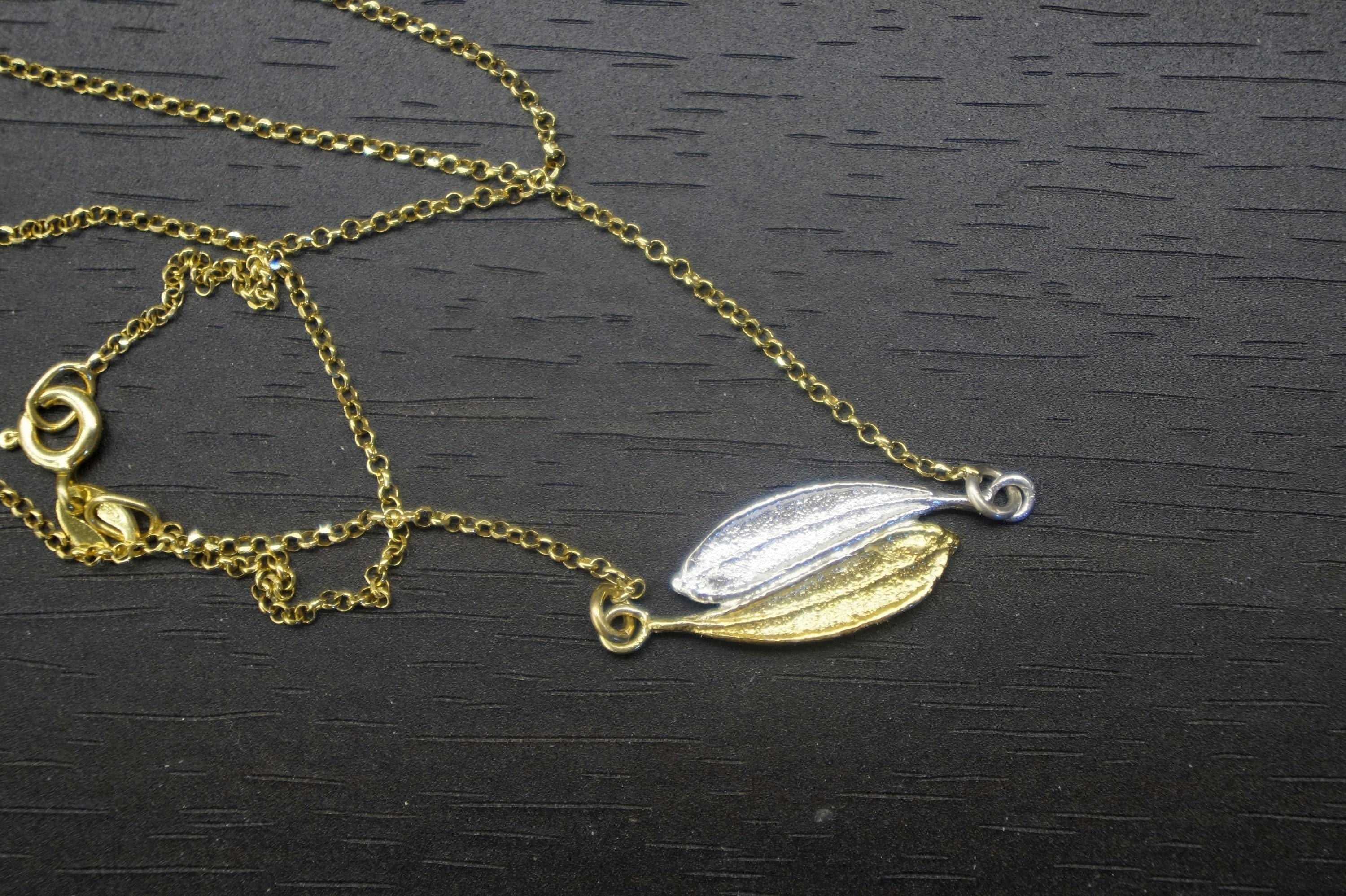 A gold and silver leaf-shaped pendant necklace is displayed on a dark surface.