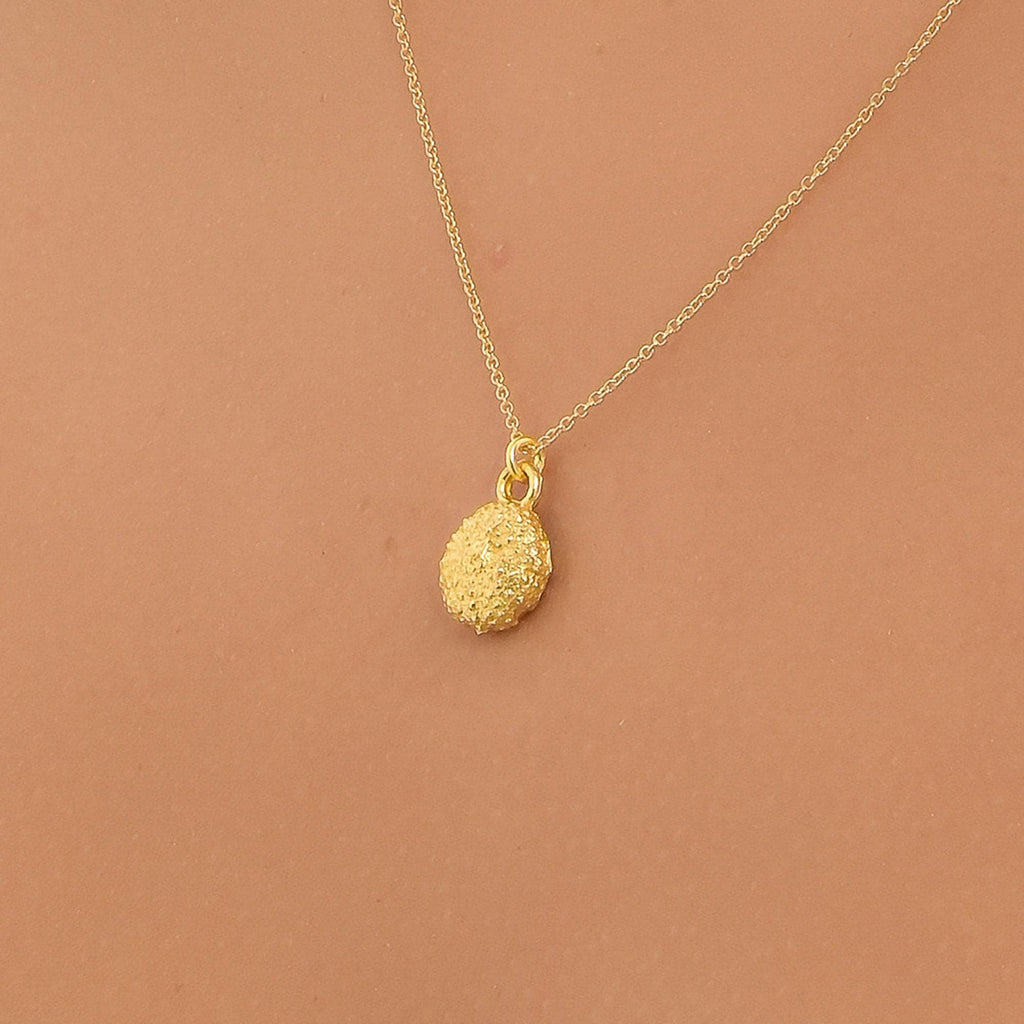 A gold necklace with a round pendant is shown against a peach-colored background.