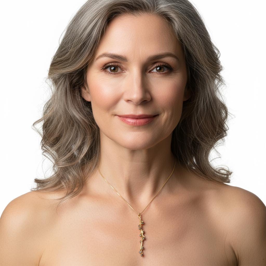 A woman with long, wavy gray hair and a warm smile, wearing a gold necklace with a pendant.