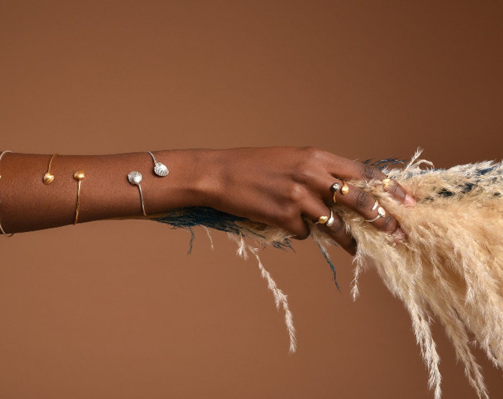 A close-up view of a person's hand wearing multiple rings and bracelets, with a fluffy white object in the background.